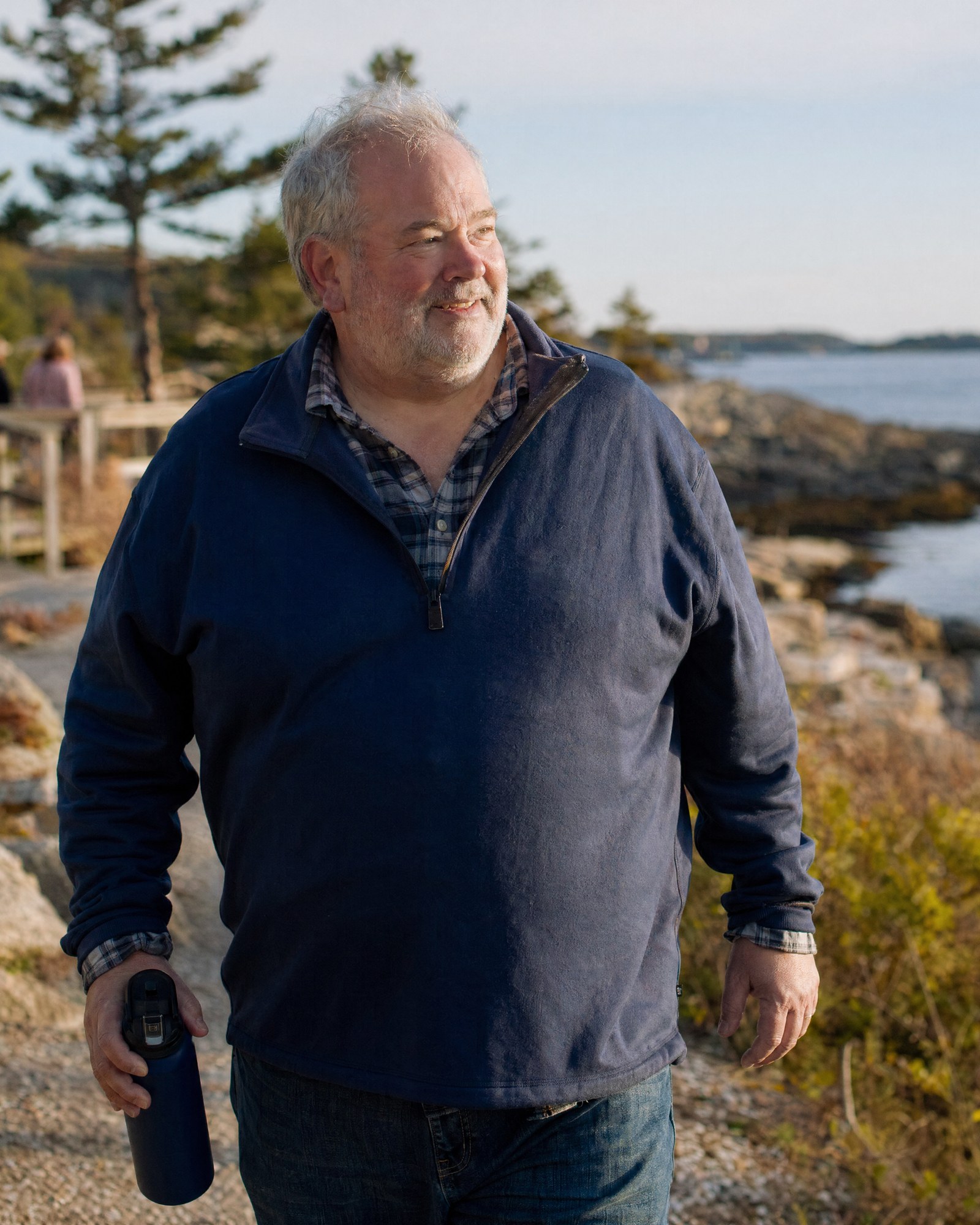 An older man walking along a coastal trail in warm late-afternoon light