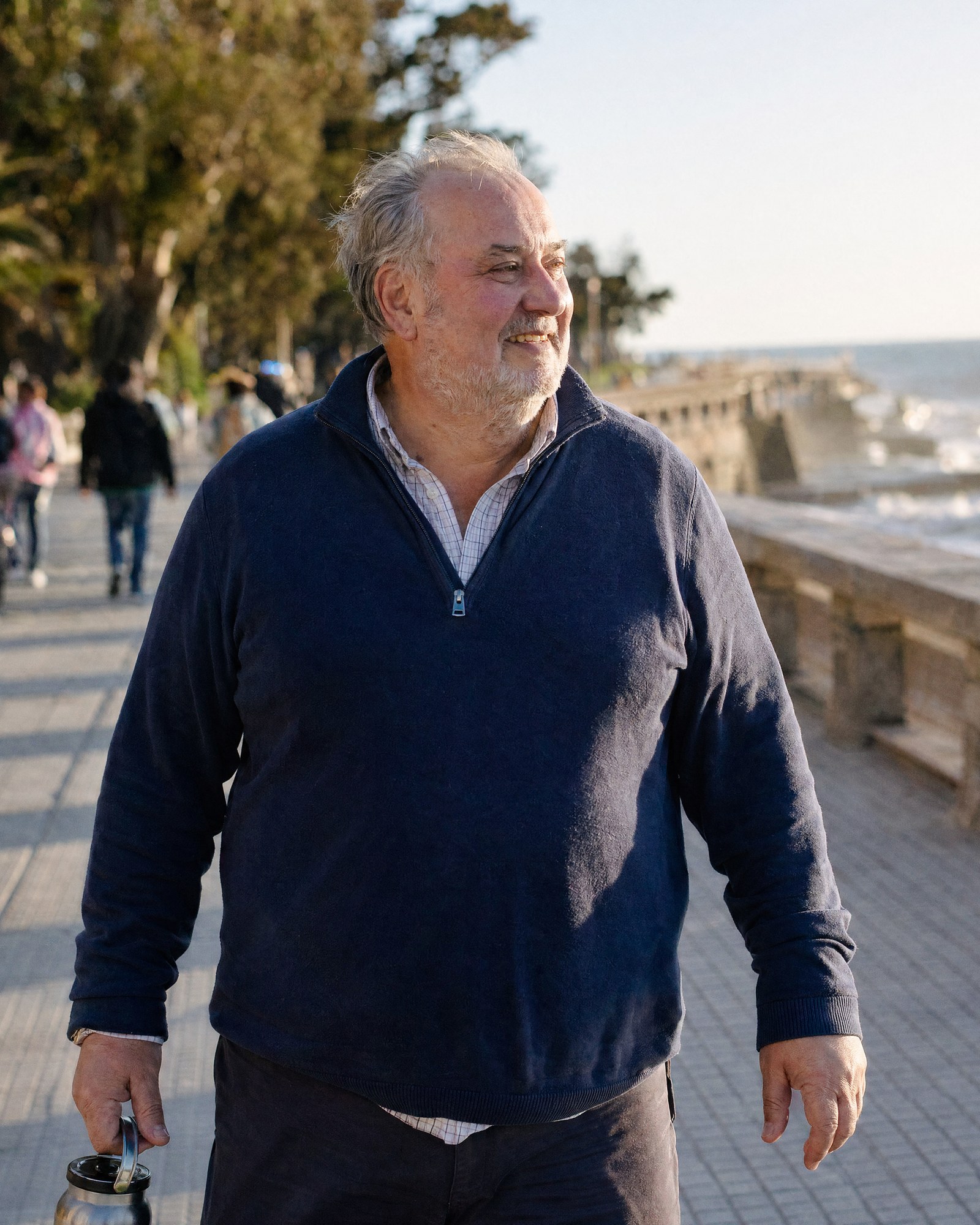 Un hombre mayor pasea por el malecón con la luz cálida del atardecer