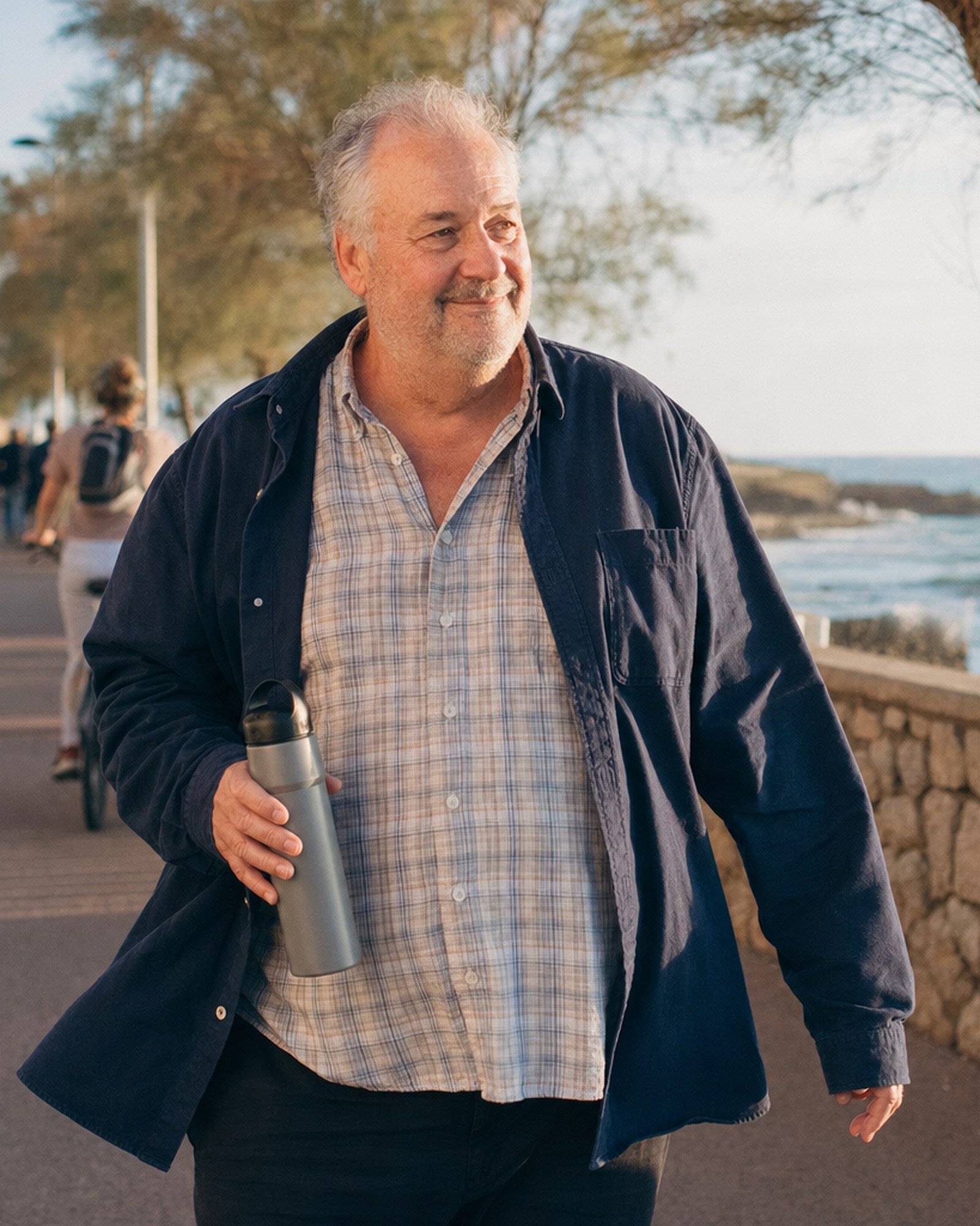 Un homme d'un certain âge marchant au bord de la mer dans la lumière chaude de l’après-midi